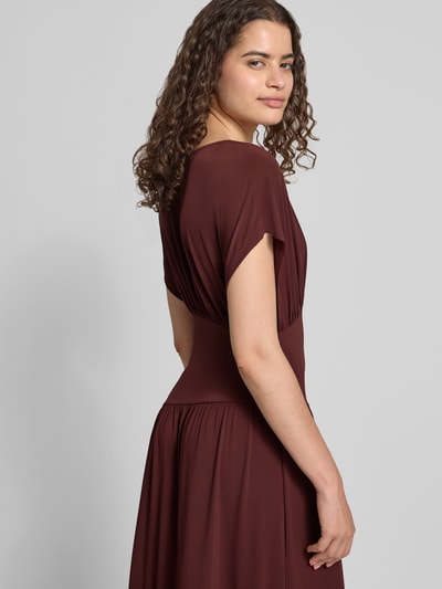 Frauenmodel trägt Maxikleid mit V-Ausschnitt von Gina Tricot in Braun, tailliert, Falten-Optik, Kappärmel, elastischer Material-Mix, Nahaufnahme Oberkörper schräg von hinten.