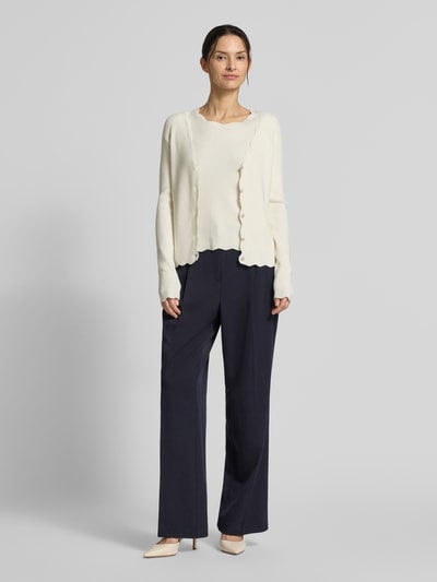 Frauenmodel trägt Strickcardigan aus Viskose-Mix von Christian Berg Woman in Offwhite mit Rüschen und Knopfleiste, taillierter Schnitt, Ganzkörperansicht von vorne.
