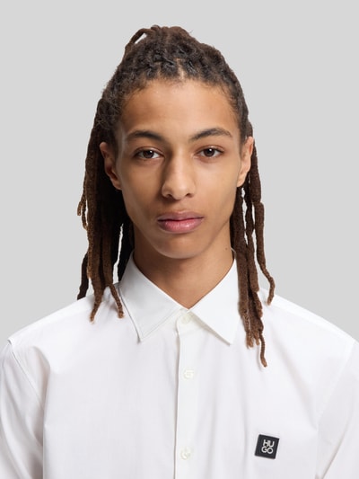 Männermodel trägt Slim Fit Freizeithemd aus Baumwoll-Mix Modell 'ERMO' von HUGO, weiß, Label Patch, Kentkragen, Nahaufnahme Oberkörper.