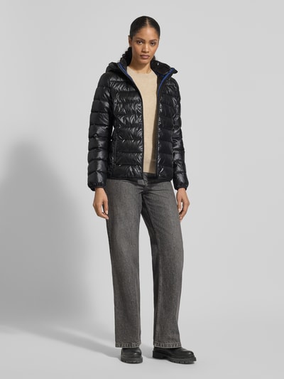 Frauenmodel trägt schwarze Jacke mit Kapuze von NAUTGÅRD, lockerer Schnitt, Tunnelzug, verdeckter Reißverschluss, Ganzkörperansicht von vorne.