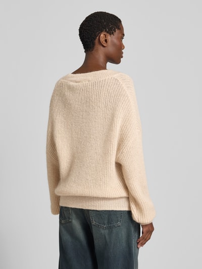 Frauenmodel trägt Oversized Pullover mit Woll-Anteil von ROTATE in beige, Strick-Optik, Logo-Patch, Material-Mix, Rückenlänge 70 cm, Ganzkörperansicht Rückansicht.