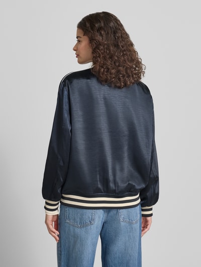 Frauenmodel trägt Bomber Jacke mit Logo-Stitching Modell 'VARSITY' von Superdry in Satin mit Lockerer-Schnitt, Rückenansicht.