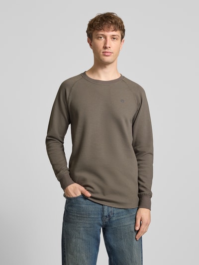 Męski model nosi Longsleeve mit Strukturmuster und Logo od G-Star Raw w kolorze brązowym, krój regular fit, bawełna, logo na piersi, widok całej sylwetki z przodu.