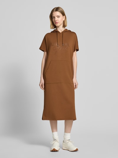 Frauenmodel trägt Sweatkleid mit Kapuze von Soyaconcept in Braun, Material-Mix mit Modal-Anteil, Gerader-Schnitt, Midikleid, Label-Print, Ganzkörperansicht von vorne.