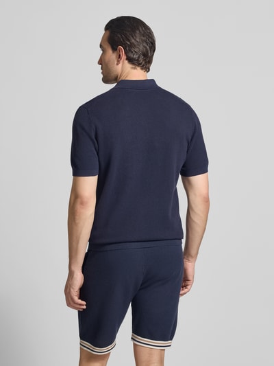 Męski model nosi Koszulkę polo o kroju slim fit z fakturowanym wzorem Model 'Johan' od Christian Berg Men, z krótkim rękawem, wykonana z bawełny, kołnierzyk polo, długość tyłu 74 cm w rozm. M, długość rękawów 24 cm w rozm. M, ciemnoniebieski, fakturowana powierzchnia, widok całej sylwetki z tyłu