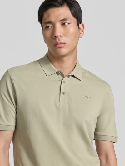 Männermodel trägt Regular Fit Poloshirt aus reiner Baumwolle Modell 'DONOS222' von HUGO in hellem Beige, feine Webstruktur, Label-Applikation, Nahaufnahme Oberkörper.