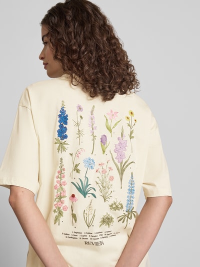 Frauenmodel trägt T-Shirt im Oversize-Fit mit Blumen-Backprint von REVIEW aus Reine Baumwolle in Creme mit Label-Details, Ganzkörperansicht Rückansicht.