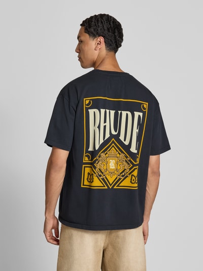 Männermodel trägt T-Shirt mit Label-Print von RHUDE, schwarze Farbe, Reine Baumwolle, Gerader-Schnitt, Kurzärmelig, Ganzkörperansicht Rückansicht.