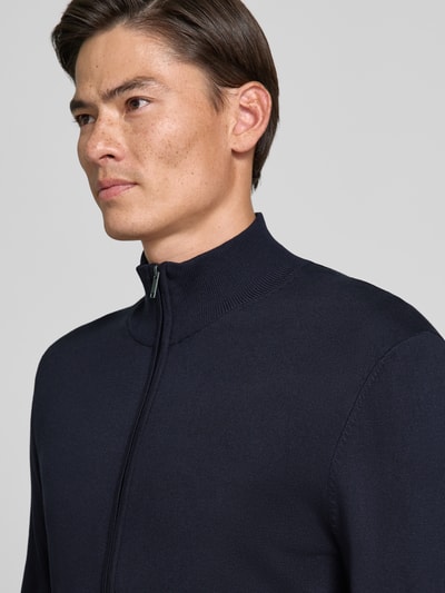 Männermodel trägt Slim Fit Strickjacke aus Viskose-Mix mit Stehkragen von MCNEAL in Dunkelblau, Nahaufnahme Oberkörper. Rückenlänge und Ärmel bei Größe M jeweils 70 cm, Reißverschluss und elastische Abschlüsse.