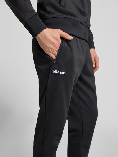 Mężczyznę model nosi spodnie dresowe z mieszanki bawełny Ellesse Sweatpants mit elastischem Bund Modell 'BERTONI', krój regular fit, detal z logo, kolor czarny, długość wewnętrzna nogawki w rozmiarze M: 76 cm, detailaufnahme obrębu bioder