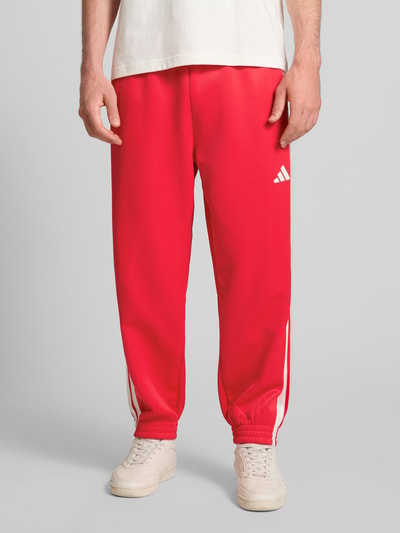 Männermodel trägt Sweatpants mit Logo und elastischem Bund von adidas Sportswear in Rot mit weißen Details, Regular Fit, Nahaufnahme Oberkörper.