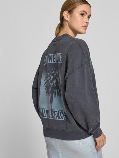 Frauenmodel trägt Regular Fit Sweatshirt mit Logo-Print von Anine Bing aus reiner Baumwolle in Anthrazit mit großem Palmenmotiv und elastischen Abschlüssen, Rückenlänge bei Größe S 62 cm, Ganzkörperansicht Rückansicht.
