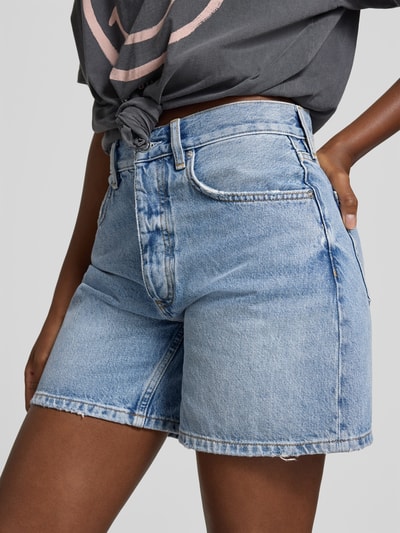 Frauenmodel trägt Regular Fit Shorts in Denim-Optik von Anine Bing aus reiner Baumwolle, 5-Pocket-Design, Knopf- und Reißverschluss, Nahaufnahme Oberkörper.
