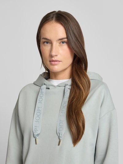 Vrouwenmodel draagt Regular Fit Hoodie met Logo-Applikation van JOOP!, katoenmix, elastische boorden, detailopname bovenlichaam.