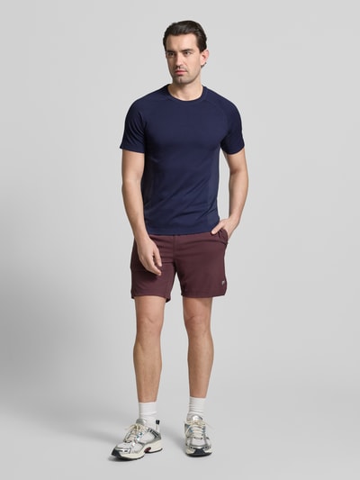 Męski model nosi Regular Fit T-Shirt mit Logo-Print von Fabletics, krój regular fit, okrągły dekolt, krótki rękaw, długość pleców w rozmiarze M: 67 cm, widok całej sylwetki z przodu.