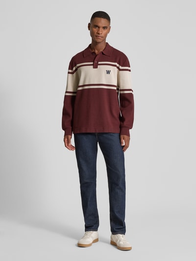 Männermodel trägt Poloshirt mit Label-Stitching Modell 'Curt' von Wood Wood in Bordeaux und Beige, lockerer Schnitt, Baumwolle, Ganzkörperansicht von vorne.