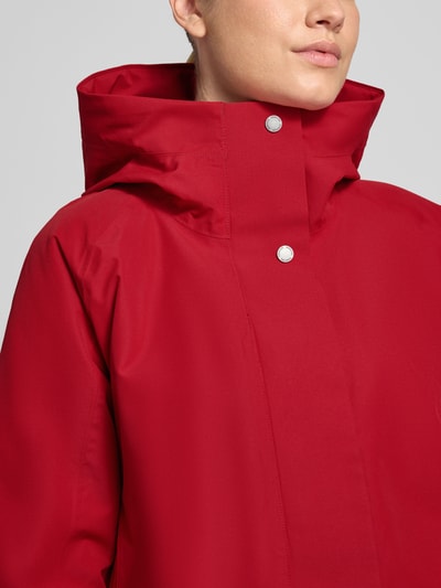 Vrouwenmodel draagt felrode parka met capuchon, gladde stof, zilverkleurige drukknoopsluiting, Regular fit. Regular Fit Parka met Capuchon Model 'Alana' van Didriksons, Steekzakken, Ruglengte maat 36: 90 cm, Schouderbreedte 38 cm, Borstwijdte 48 cm, Mouwlengte 74 cm. Nahaufnahme bovenlichaam.