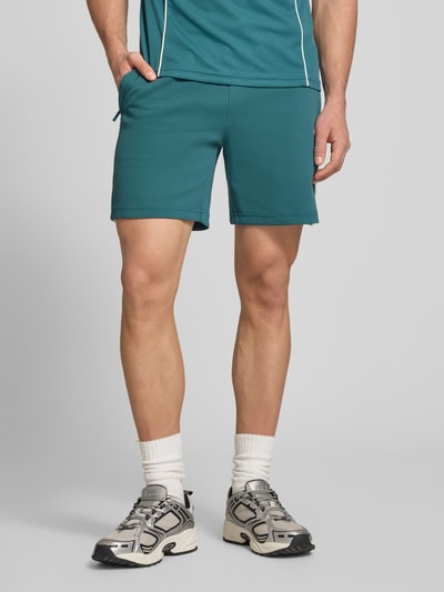 Männermodel trägt Shorts mit Logo-Stitching Modell 'EGEO' von SERGIO TACCHINI in Dunkelgrün, Baumwoll-Mix, lockerer Schnitt, Ganzkörperansicht von vorne.