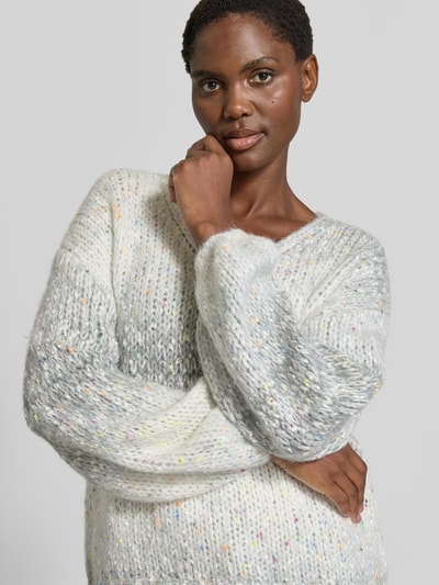 Kobiece modelka ma na sobie sweter z dzianiny Strickpullover aus Effektgarn mit V-Ausschnitt von Apricot, Mieszanka materiałów z dodatkiem wełny, krój regular fit, efektowna przędza, dekolt w serek, długość tyłu w rozmiarze S: 46 cm, długość rękawów w rozmiarze S: 49 cm, widok na górną część ciała z przodu.