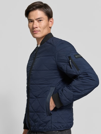 Männermodel trägt Regular Fit Bomberjacke mit Ärmeltasche von Tom Tailor in Dunkelblau mit Rautenstepp, seitliche Eingrifftaschen, Nahaufnahme Oberkörper.
