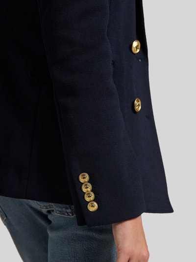 Frauenmodel trägt Zweireihiger Blazer mit Woll-Anteil von Polo Ralph Lauren in Dunkelblau mit goldenen Knöpfen und Pattentaschen, Detailaufnahme Ärmel.