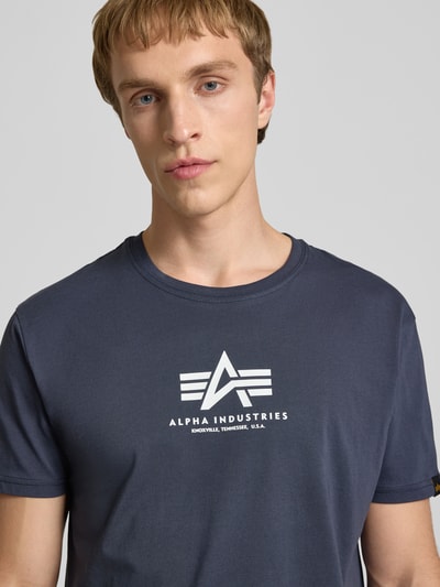 Mannelijk model draagt T-shirt met logo en ronde hals van Alpha Industries, puur katoen, regular fit, ruglengte maat M 67 cm, nahaufnahme bovenlichaam.