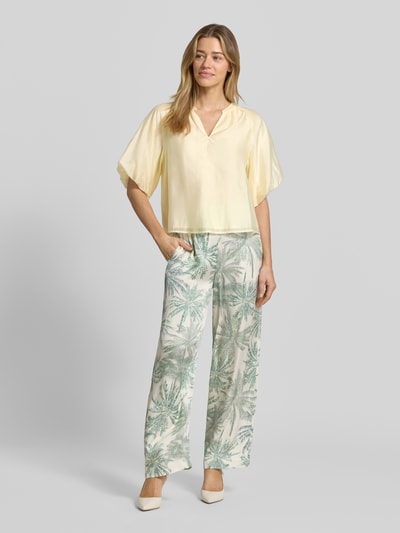 Frauenmodel trägt Loose Fit Blusenshirt aus Lyocell-Mix von s.Oliver BLACK LABEL in Optik: Unifarben, Passform: Loose-Fit, V-Ausschnitt, Raffung, Puffärmel, Raglanärmel, Ärmelabschluss elastisch, Material: Lyocell-Mix, sanft schimmernder Stoff, zart gelb, glatte Textur, Ganzkörperansicht von vorne.