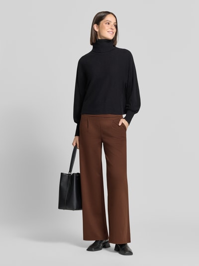 Frauenmodel trägt Wide Fit Hose mit Viskose-Anteil Modell 'Kate' von ICHI in Braun mit Bundfalten und Eingrifftaschen, Ganzkörperansicht von vorne.