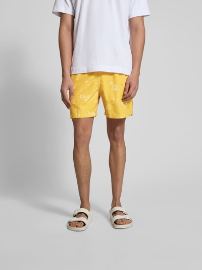Männermodel trägt Badehose mit Eingrifftaschen von Closed in Gelb mit weißen Motiven, elastischer Bund, Gerade Passform, Ganzkörperansicht von vorne.