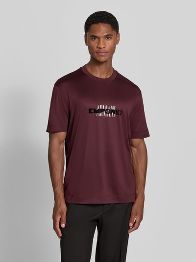 Männermodel trägt T-Shirt mit Label-Print von Emporio Armani in Bordeaux, Lyocell-Baumwoll-Mix, gerader Schnitt, Rundhalsausschnitt, Ganzkörperansicht von vorne.