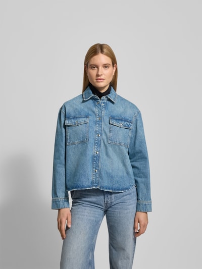 Vrouwenmodel draagt Regular Fit Overhemdblouse in denimlook van Anine Bing, puur katoen, borstzakken, knoopsluiting, Ganzkörperansicht von vorne. Ruglengte maat S: 67 cm, borstwijdte: 62 cm, mouwlengte: 59 cm.