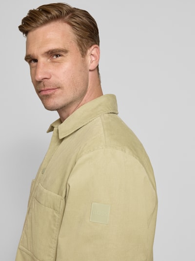 Männermodel trägt Regular Fit Hemdjacke aus Baumwoll-Mix Modell 'Locky_2_M' von BOSS Orange in Beige mit sichtbarer BOSS-Logo-Applikation, Nahaufnahme Oberkörper.