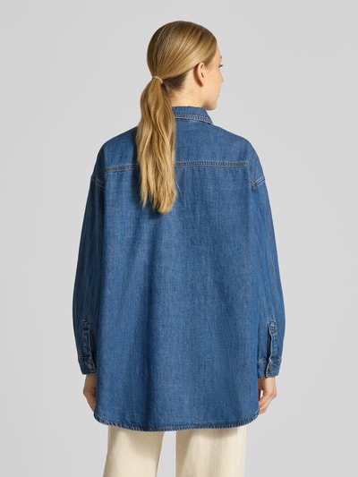 Frauenmodel trägt Oversized Jeansbluse mit überschnittenen Schultern Modell 'Hilma' von My Essential Wardrobe, reine Baumwolle, mittleres Blau, lockere Passform, strukturierte Denim-Oberfläche, Umlegekragen, Rückenlänge 80 cm, Ärmellänge 52 cm, Ganzkörperansicht Rückansicht.