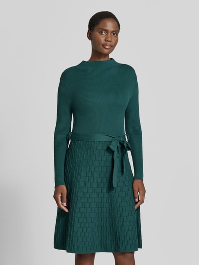 Modelka nosi Knielanges Strickkleid mit Bindegürtel von Apricot, Mieszanka wiskozy, Linia a, Długość do kolan, stójka, wiązany pasek, Długość tyłu w rozmiarze S: 103 cm, Szerokość w rozmiarze S: 38 cm, Długość rękawów w rozmiarze S: 59 cm, Zielony, faktura pleciona, widok na cały przód,