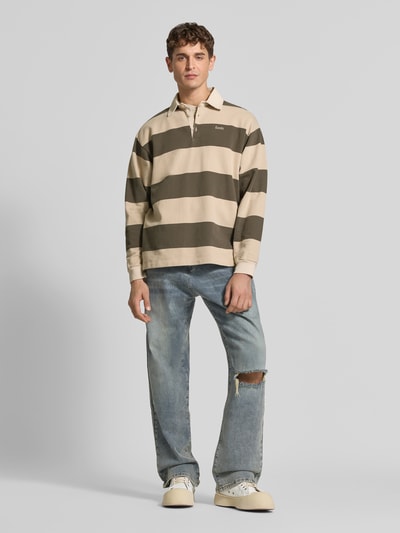 Männermodel trägt Sweatshirt mit Label-Stitching von Forét mit breiten beige-olivgrünen Streifen, gerader Schnitt, Polokragen, Ganzkörperansicht von vorne. Rückenlänge bei Größe M: 72 cm, überschnittene Schultern, Produkt für Herren.