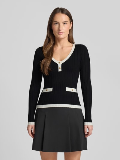 Frauenmodel trägt Slim Fit Longsleeve aus Viskose-Mix Modell 'Laurel' von Guess in Schwarz mit Zierknöpfen, Strick-Optik, Ganzkörperansicht von vorne. Rückenlänge bei Größe S: 52 cm, Ärmellänge bei Größe S: 63 cm, Rundhalsausschnitt.