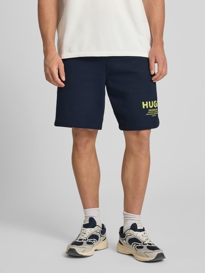 Männermodel trägt Loose Fit Sweatshorts aus reiner Baumwolle Modell 'NOMARIO' von Hugo Blue, unifarben, Logo Print, Nahaufnahme Oberkörper.