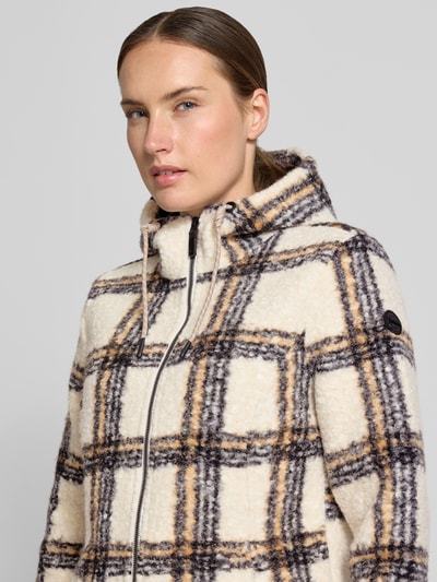 Frauenmodel trägt Mantel aus Teddyfell von G.I.G.A. DX, kariertes Muster in Beige, Braun und Schwarz, Kapuze mit Tunnelzug, Nahaufnahme Oberkörper.