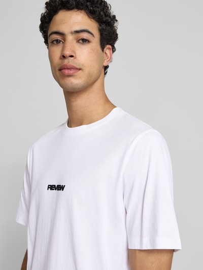Męskimodel nosi T-Shirt mit Logo und Rundhalsausschnitt od REVIEW, biała bawełna, krój relaxed fit, długość tyłu 68 cm, zbliżenie na górną część ciała.