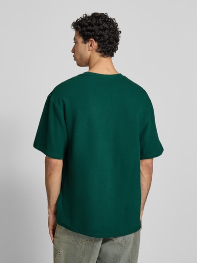 Männermodel trägt Oversized T-Shirt mit Logo-Stitching von KARL KANI in Grün aus Reine Baumwolle, Oversized-Fit, Rundhalsausschnitt, Rückenlänge 73 cm bei Größe M, Ganzkörperansicht Rückansicht.