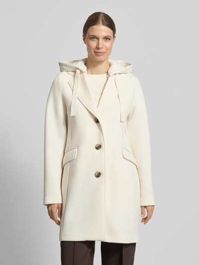 Modelka nosi Płaszcz mit Kapuze und Pattentaschen von Christian Berg Woman Selection, mieszanka materiałów z dodatkiem wiskozy, krój regular fit, kaptur z tunelem, listwa guzikowa, kieszenie z patką, długość tyłu w rozmiarze 36: 88 cm, szerokość ramion w rozmiarze 36: 45 cm, szerokość klatki piersiowej w rozmiarze 36: 50 cm, długość rękawów w rozmiarze 36: 57 cm, kolor kremowy, gładka faktura, prosty kształt. Zdjęcie: widok całej sylwetki z przodu.