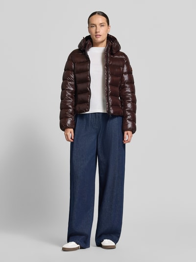 Kobieta modelka nosi kurtkę w stylu puffer z efektem pikowania Model 'Mary' od Save The Duck, kolor brązowy, taliowany krój, kaptur ze stójką, zamek błyskawiczny dwustronny, wpuszczane kieszenie z zamkiem błyskawicznym, długość tyłu w rozmiarze S: 53 cm, szerokość ramion w rozmiarze S: 44 cm, szerokość w klatce piersiowej w rozmiarze S: 41 cm, długość rękawów w rozmiarze S: 66 cm, widok całej sylwetki z przodu.