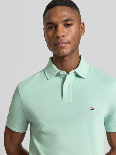 Mężczyznę model nosi Regular Fit Poloshirt aus Baumwoll-Mix von Tommy Hilfiger, efekt: jednolity kolor, krój regular fit, wyhaftowane logo, kołnierzyk polo, zapięcie na 2 guziki, krótki rękaw, wykończenie: z rozcięciem, wykończenie materiału: pika, mieszanka bawełny. Nahaufnahme Oberkörper.
