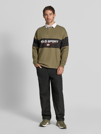 Mężczyzna nosi Relaxed Fit Poloshirt aus reiner Baumwolle von Polo Ralph Lauren, oliwkowa z czarnym i białym, Ganzkörperansicht von vorne.