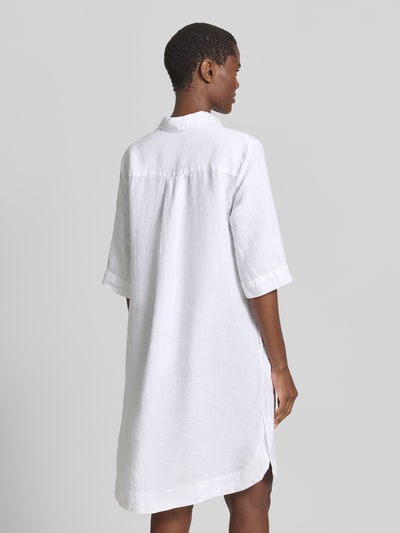 Männermodel trägt knielanges Leinenkleid Modell 'DERRY' von 0039 Italy, czysty len, prosty krój, długość do kolan, kołnierzyk koszulowy, dekolt w serek, długość tyłu w rozmiarze S: 99 cm, szerokość w rozmiarze S: 53 cm, długość rękawów w rozmiarze S: 37 cm, biała, gładka faktura, całkowita sylwetka z tyłu.