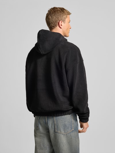 Männermodel trägt schwarzen Fleecepullover mit Reißverschluss Modell 'Olten' von Pegador, Relaxed Fit, Kapuze, Rückansicht Ganzkörperansicht.