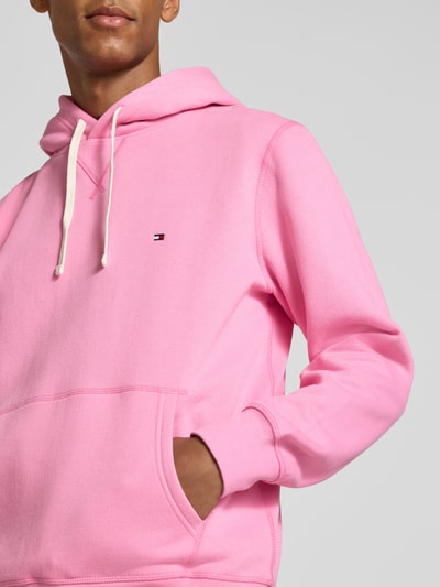 Männermodel trägt Regular Fit Hoodie aus Baumwoll-Mix von Tommy Hilfiger in Rosa mit Kängurutasche, Nahaufnahme Oberkörper.