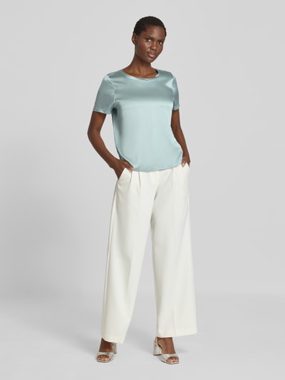 Frauenmodel trägt Blusenshirt aus Satin mit Rundhalsausschnitt von Christian Berg Woman Selection in Hellgrün, glatte Textur, Ganzkörperansicht von vorne.