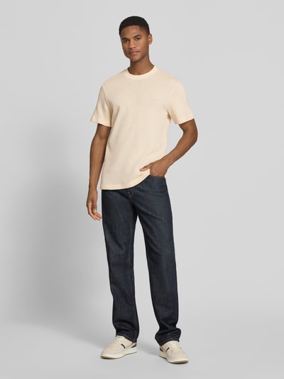 Męski model nosi Regular Fit T-Shirt aus reiner Baumwolle od Lacoste, kremowy kolor, strukturalny wzór, logo, okrągły dekolt, krótki rękaw, dzianina, bawełna, unikatowa faktura, jednolity, widok całej sylwetki z przodu.