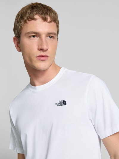 Männermodel trägt Regular Fit T-Shirt aus Baumwoll-Mix Modell 'EVOLUTION' von The North Face in Weiß mit Label-Detail, Nahaufnahme Oberkörper.